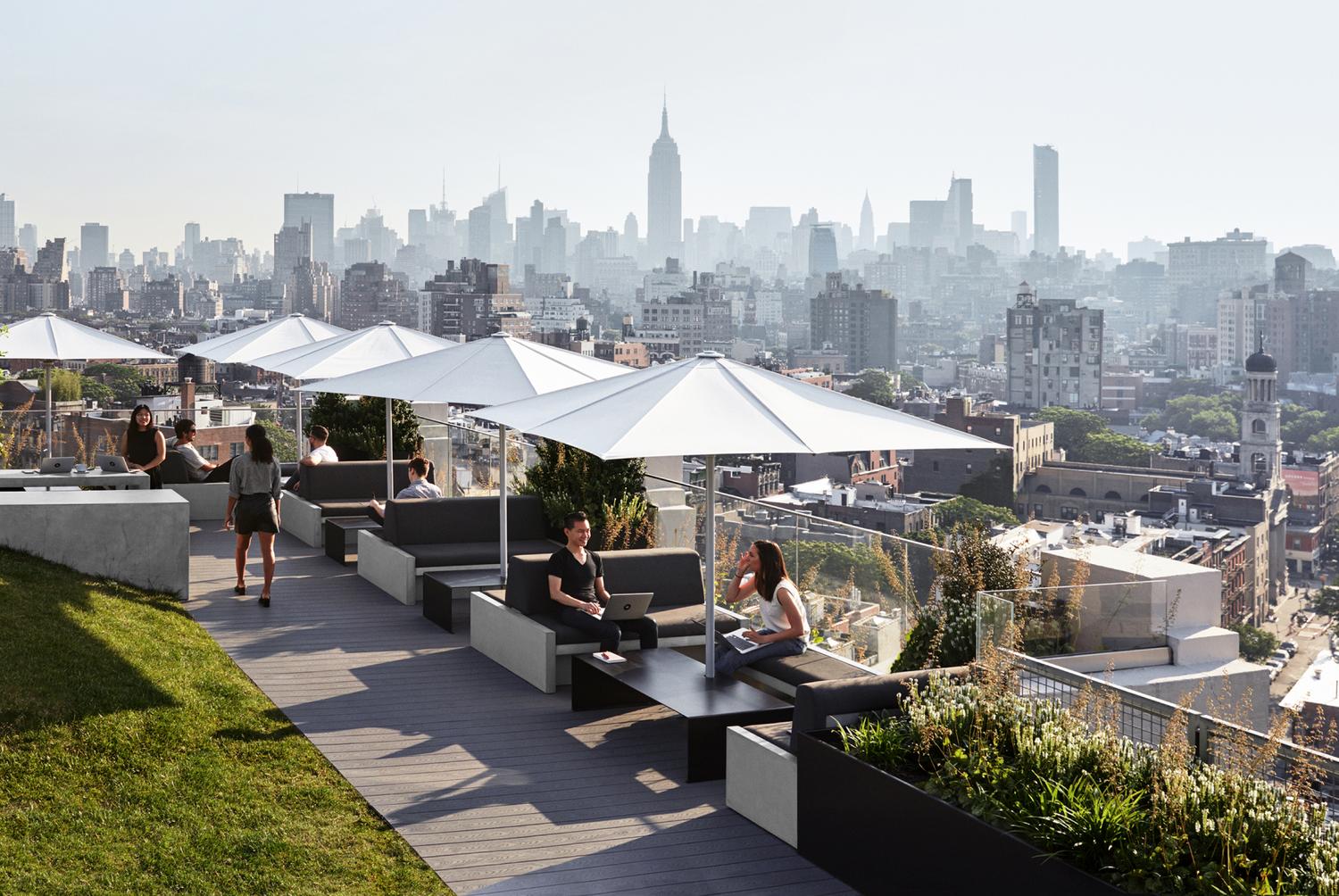 A photograph from of the Squarespace rooftop terrace with umbrella tables and several employees sitting and chatting, and in the background you can see lower Manhattan